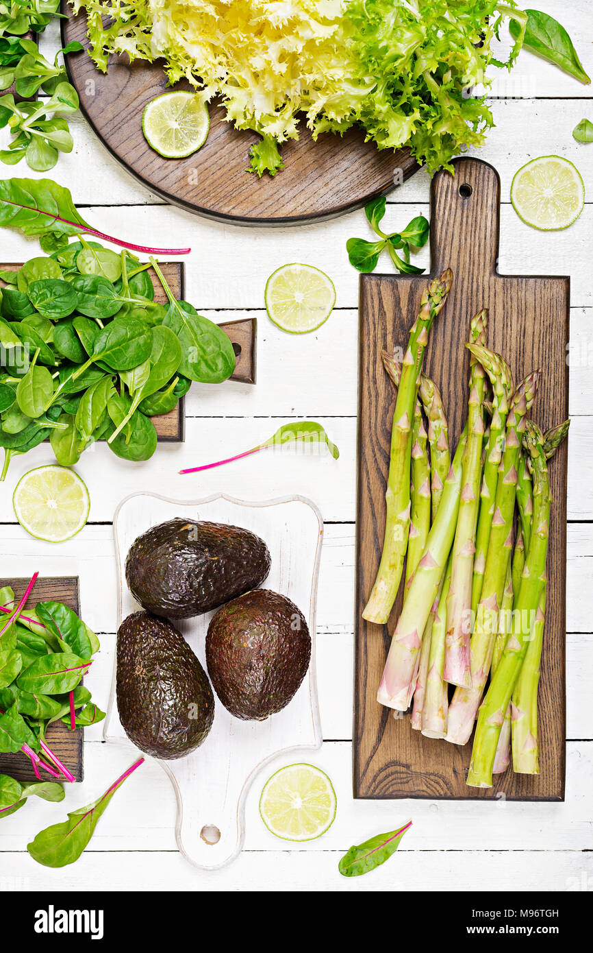 Erbe verdi, asparagi e avocado nero su bianco sullo sfondo di legno. Vista dall'alto. Lay piatto Foto Stock