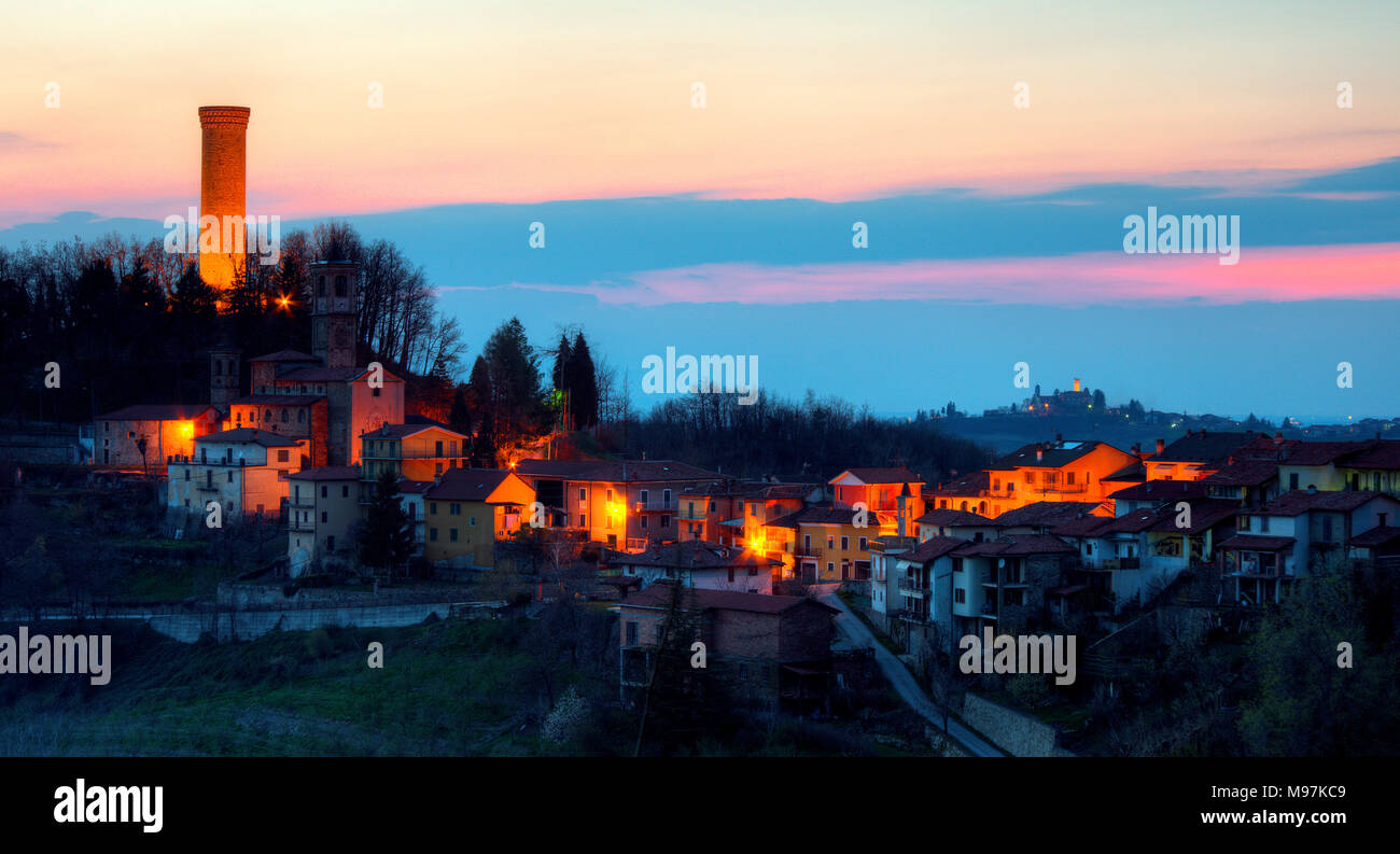Un piccolo villaggio in Italia. La notte scende sulla Castellino Tanaro nelle Langhe in Piemonte. Dietro di lui è la Rocca Ciglié, con la sua alta torre illuminata. Foto Stock