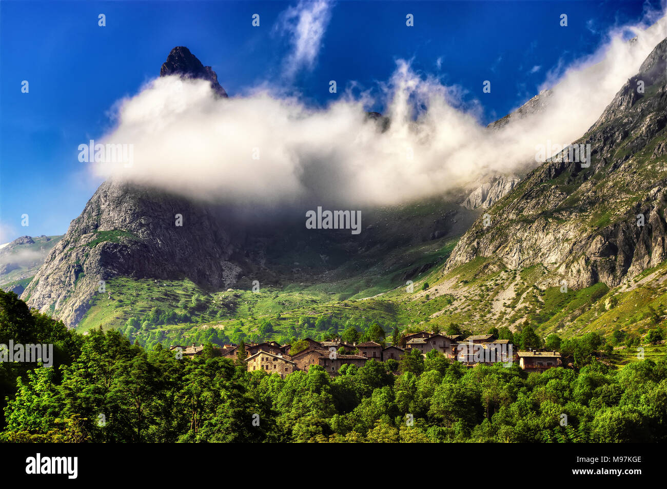 Il villaggio di Chiappera, in alta Valle Maira in Piemonte, surmonted dal Provenzale Rock, parzialmente avvolto dalle nuvole. Foto Stock