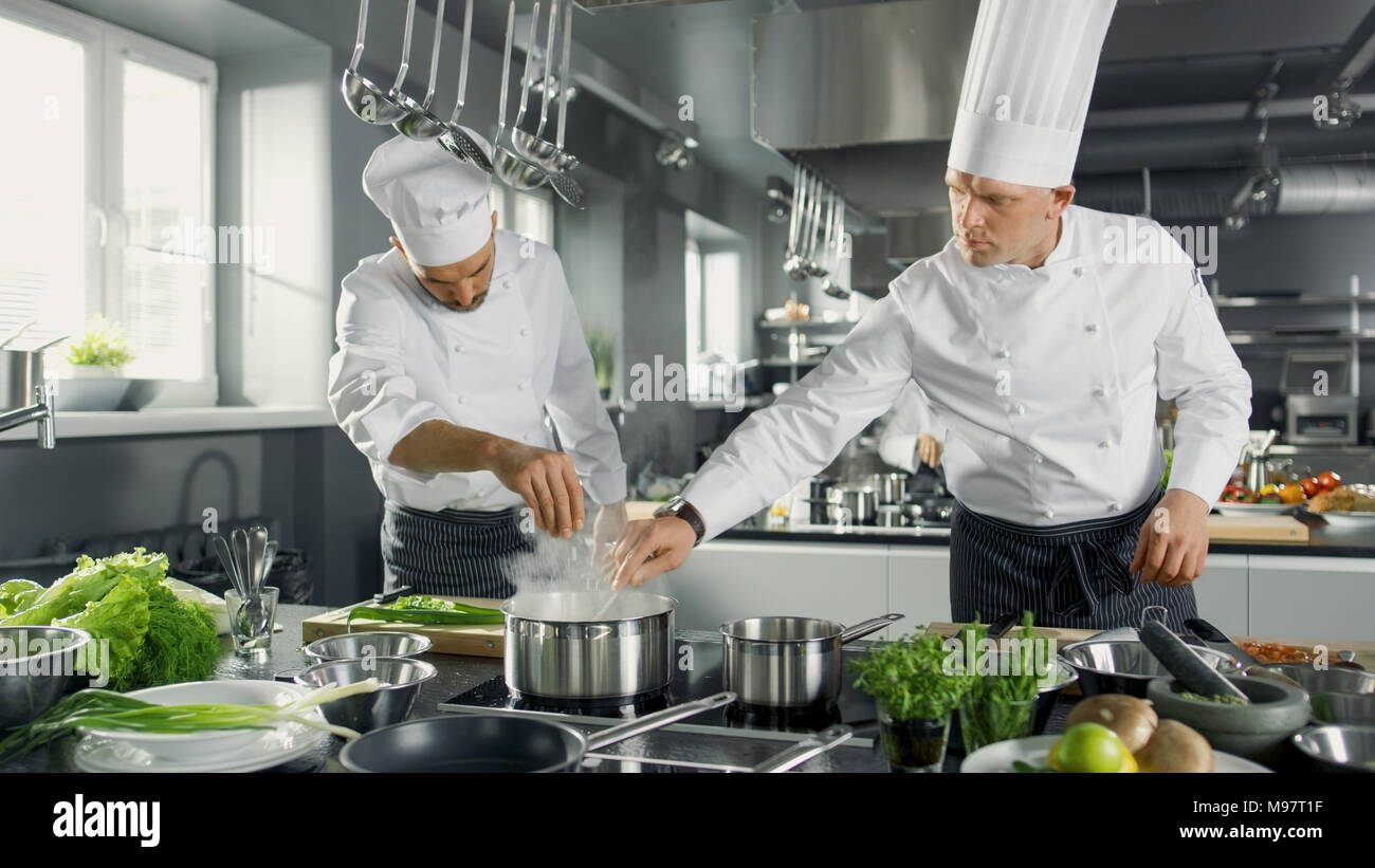 Due famosi chef lavorano come una squadra in un grande ristorante Cucina. Le verdure e gli ingredienti sono ovunque, la cucina è moderna. Foto Stock