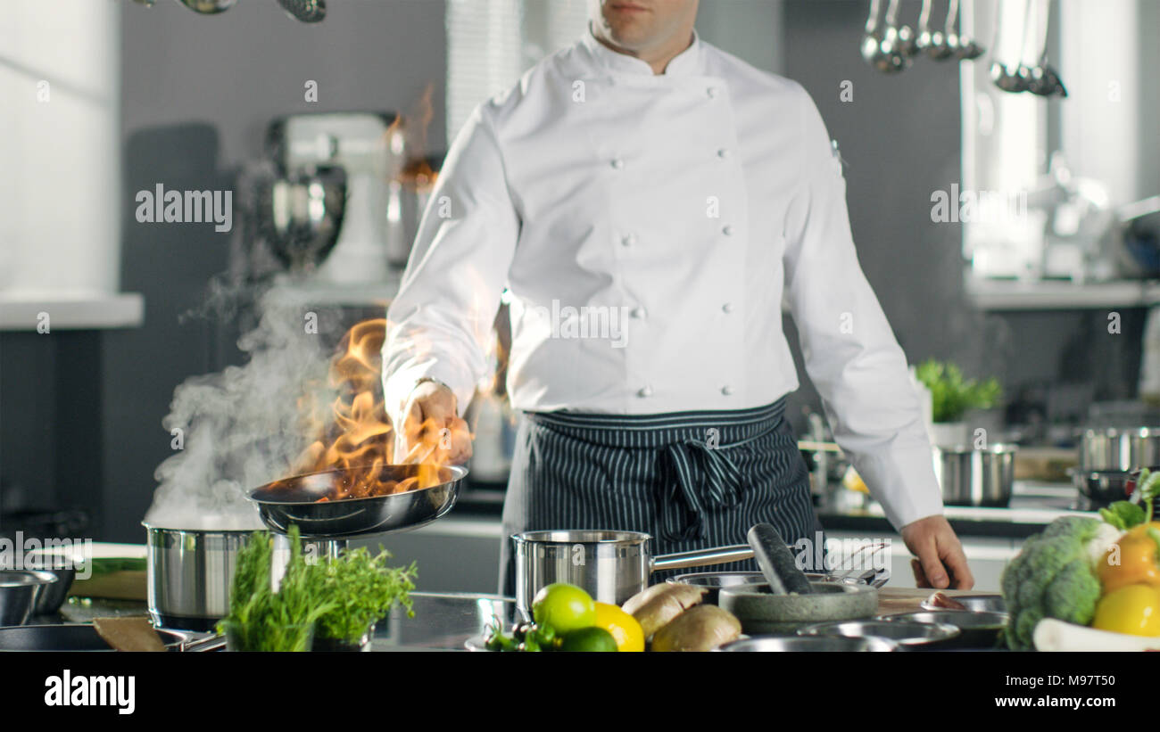 Chef professionale incendi fino olio su una padella. Flambe lo stile di cucina. Egli lavora in una cucina moderna con un sacco di ingredienti in giro. Foto Stock