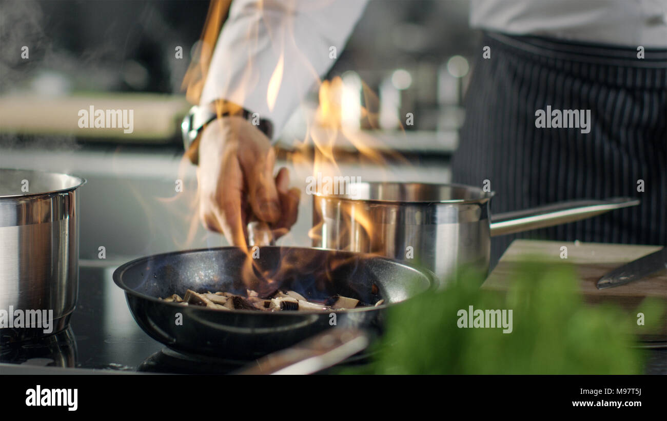 Chef professionale cuochi Flambe stile. Egli prepara il piatto in una padella con fiamme libere.Egli lavora in una cucina moderna con ingredienti diversi in giro. Foto Stock