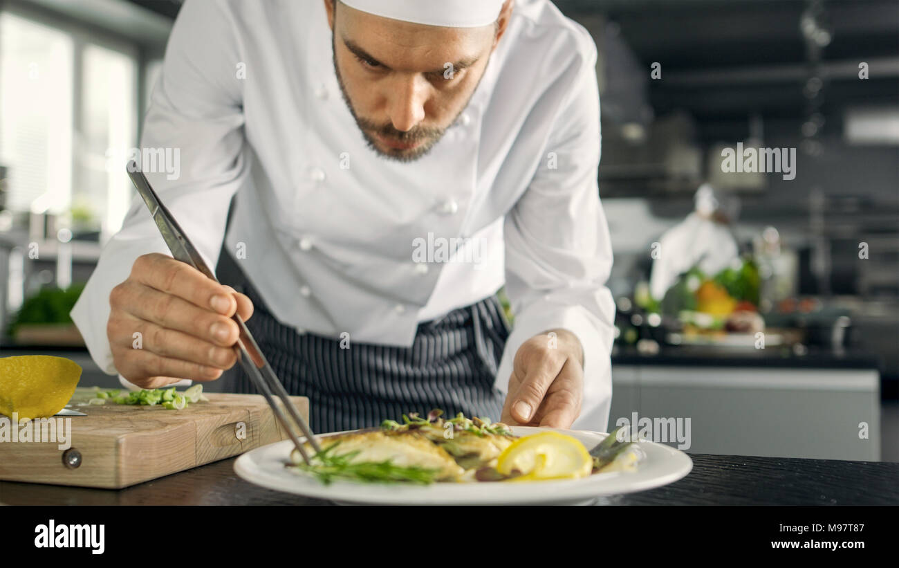 Famoso Chef decora la sua speciale piatto di pesce con un po' di verde. Egli lavora in una cucina moderna. Foto Stock
