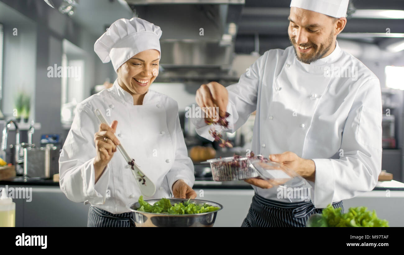 Maschio e femmina di famosi chef squadra preparare insalate per il loro ristorante a cinque stelle. Essi lavorano su un grande ristorante in Acciaio Inox cucina professionale. Foto Stock