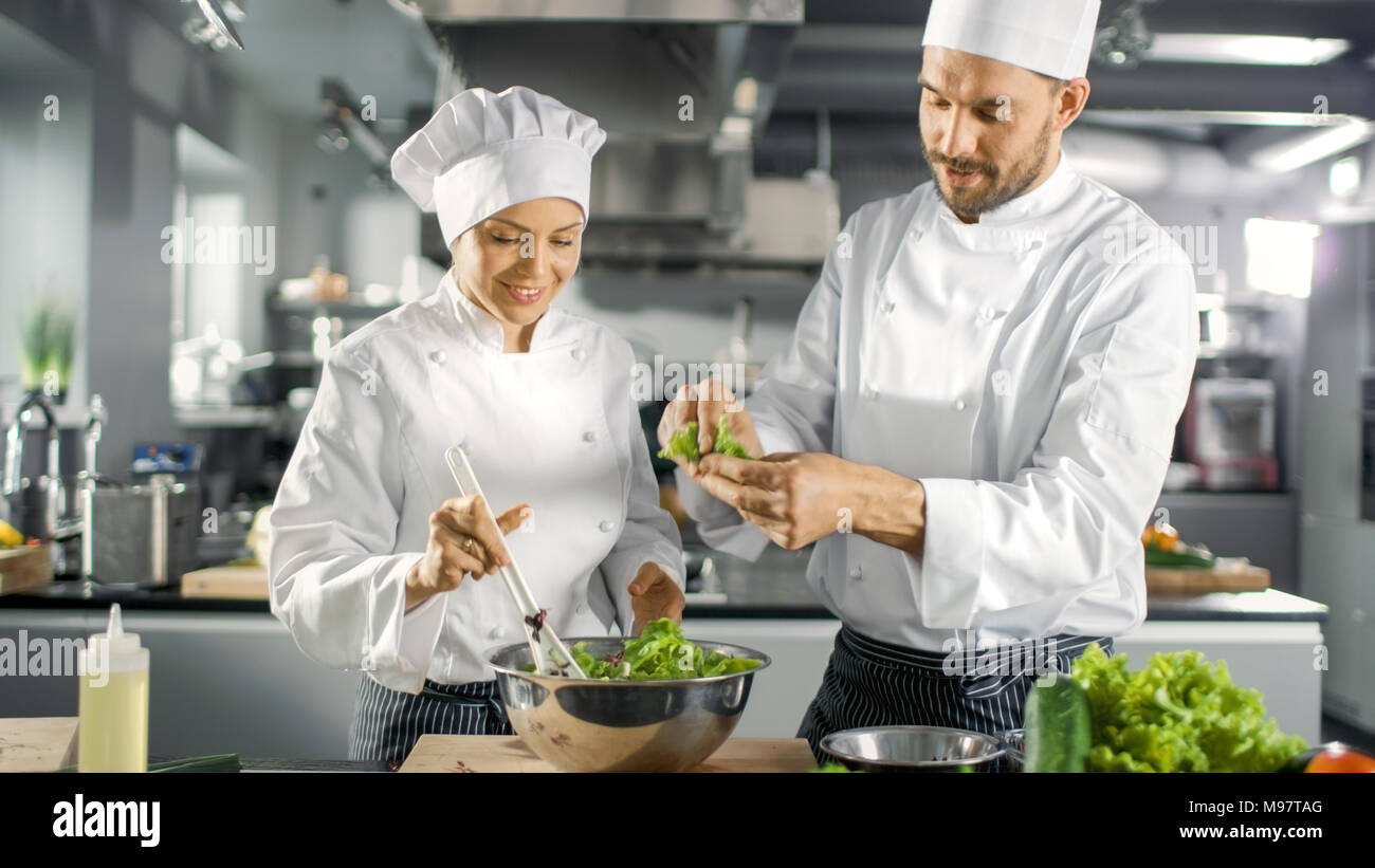 Maschio e femmina di famosi chef squadra preparare insalate per il loro ristorante a cinque stelle. Essi lavorano su un grande ristorante in Acciaio Inox cucina professionale. Foto Stock