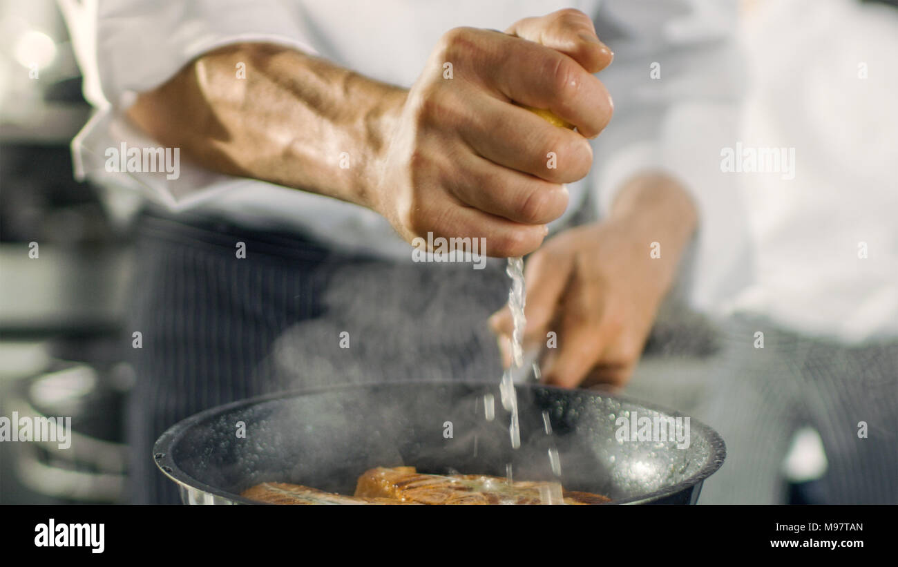 Chef professionale spreme il succo di limone sulla padella calda con rosso Filetto di pesce su di esso. Egli lavora in una cucina moderna. Foto Stock
