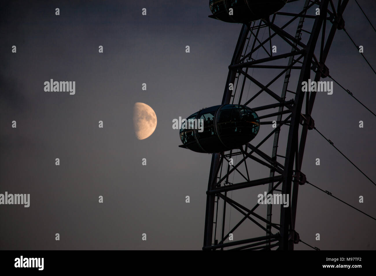 Un primo piano di una mezza luna passa dietro uno dei baccelli del London Eye appena dopo che il sole ha impostato, Londra Foto Stock