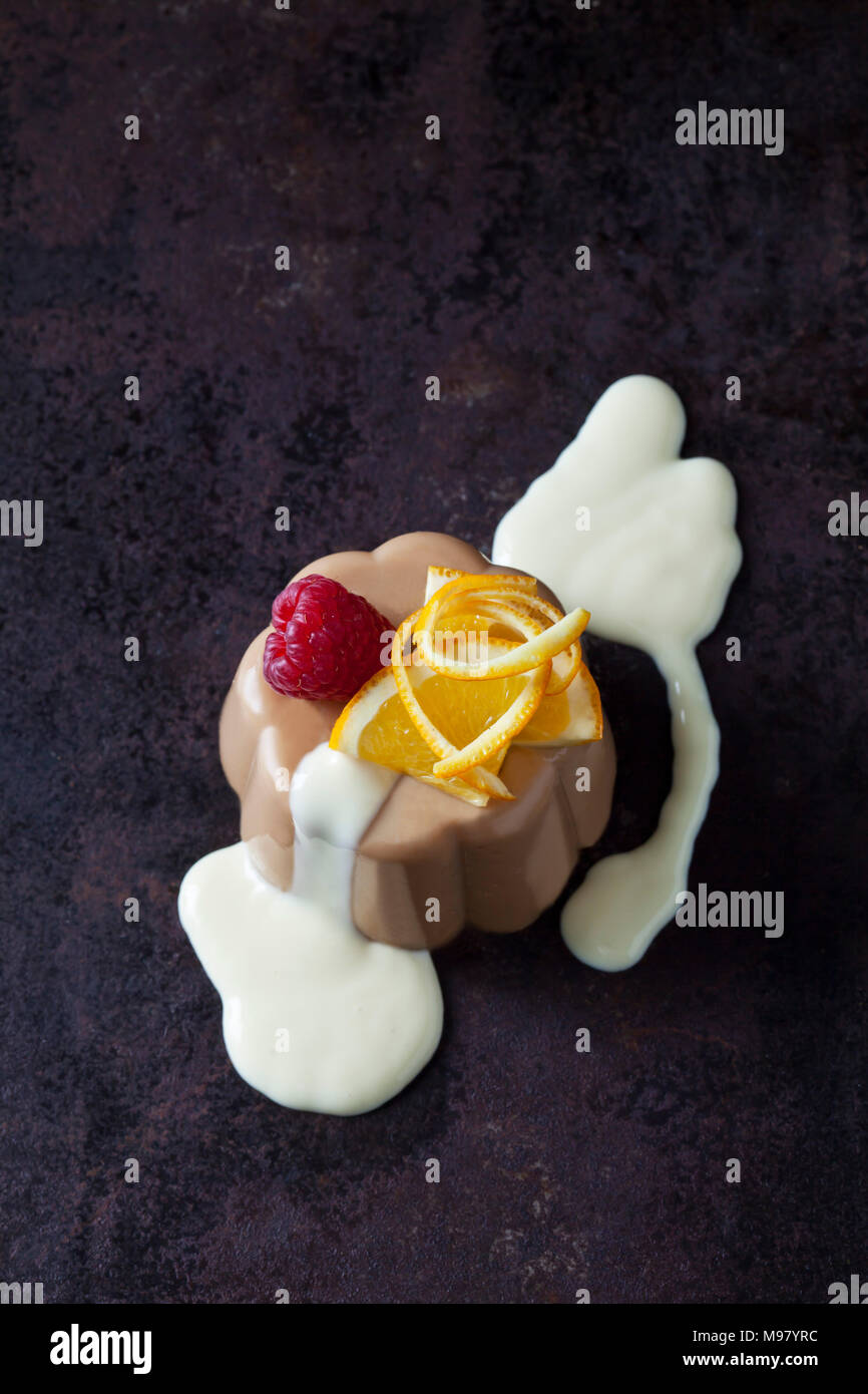 Budino di cioccolato e salsa alla vaniglia guarnita con lampone e arancione Foto Stock