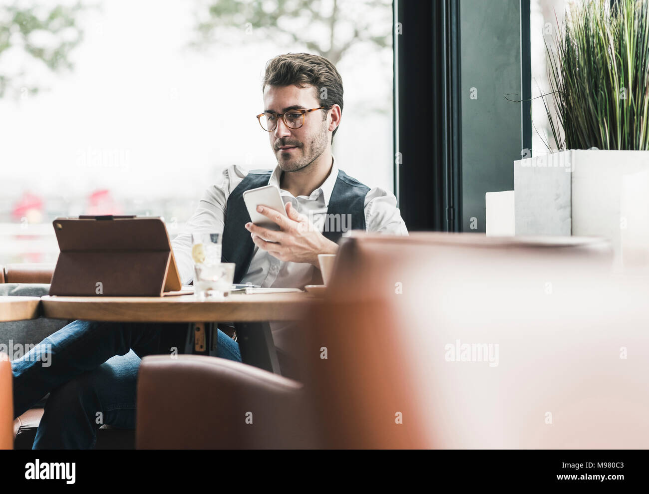 Giovane uomo che lavora in un bar con tablet e telefono cellulare Foto Stock