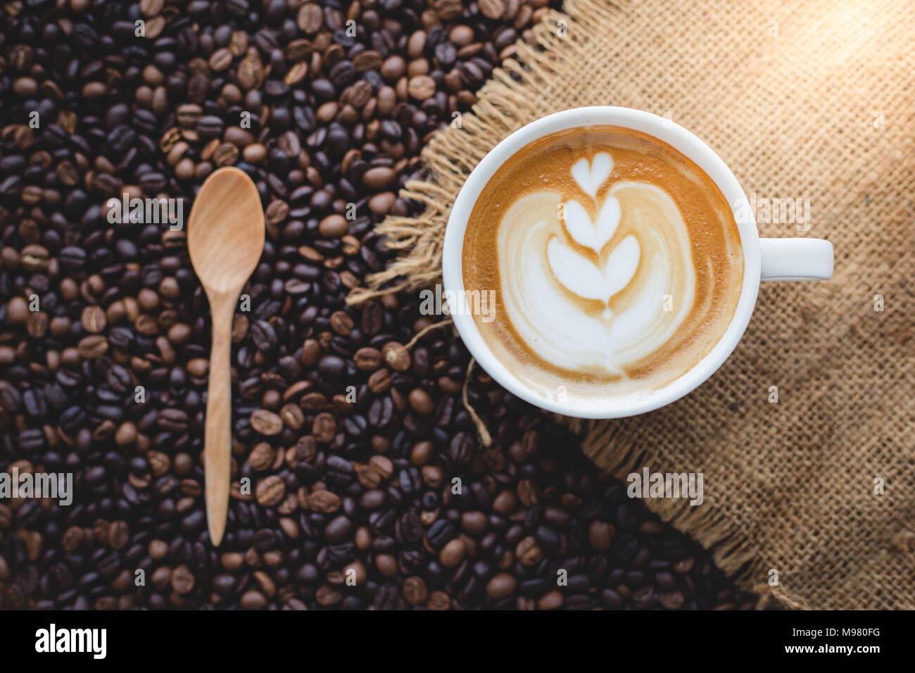Una tazza di caffè latte sul sacco con chicco di caffè e cucchiaio di legno Foto Stock
