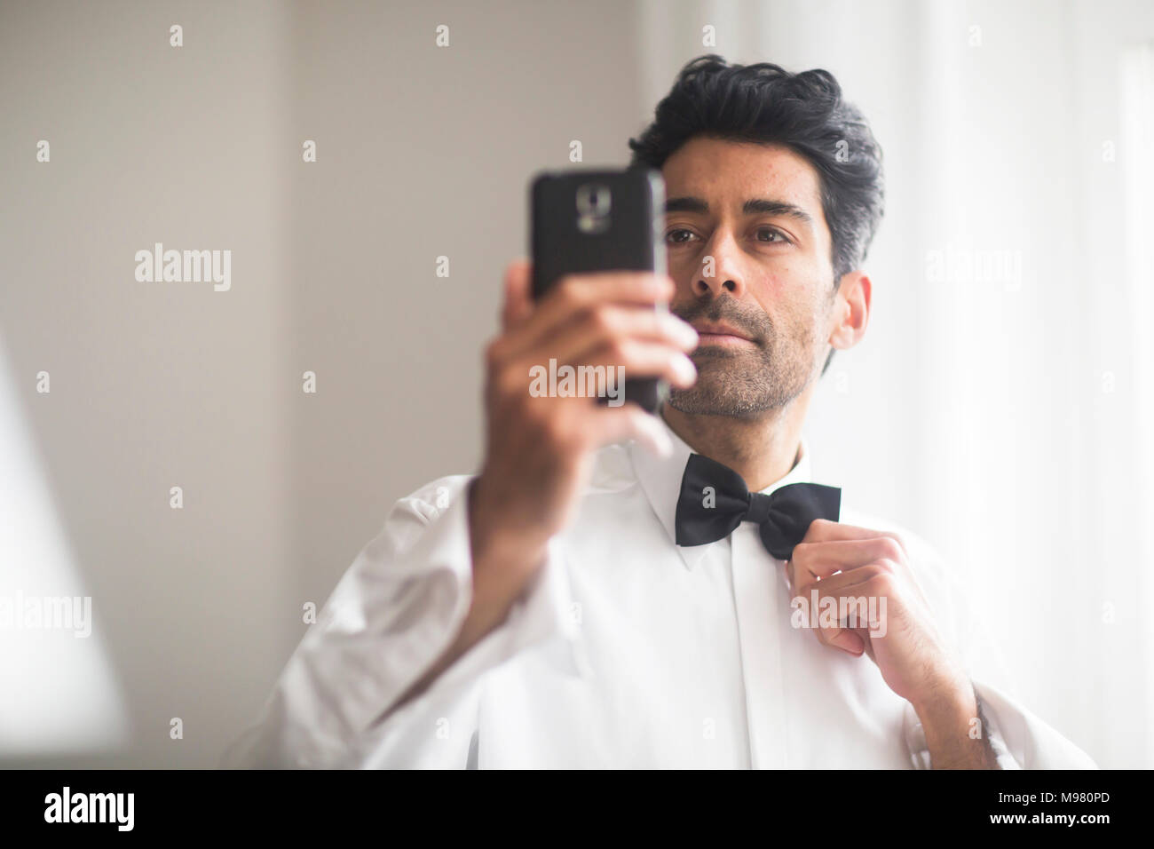 Ritratto di uomo con telefono cellulare per regolare il suo bow tie Foto Stock