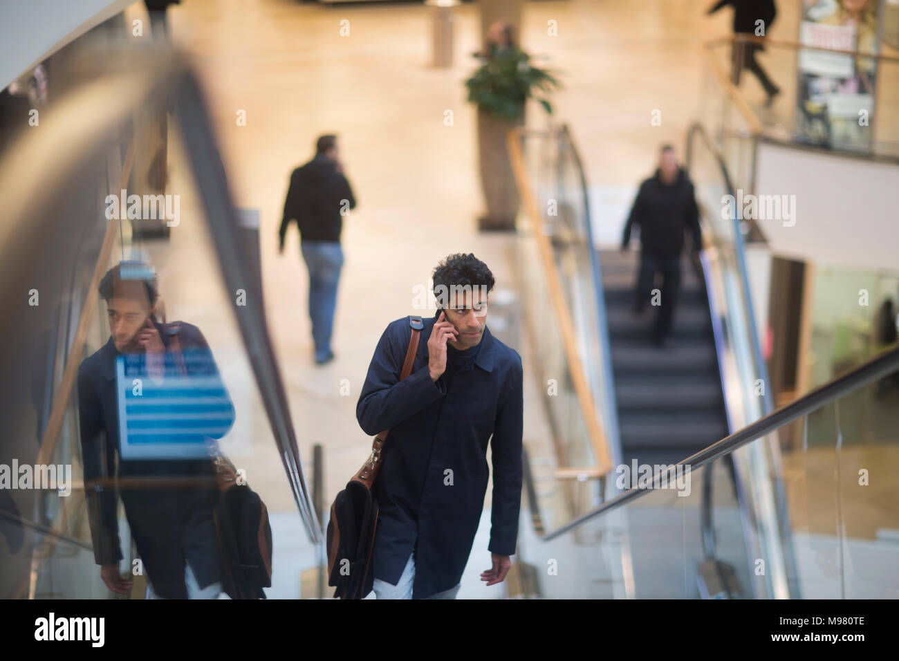 Uomo al telefono stando in piedi sulla scala mobile in un centro commerciale per lo shopping Foto Stock