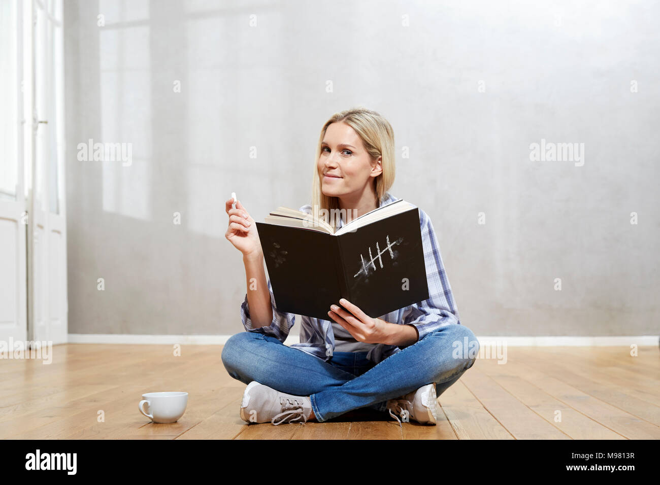 Ritratto di sorridere donna bionda con libro seduti sul pavimento Foto Stock