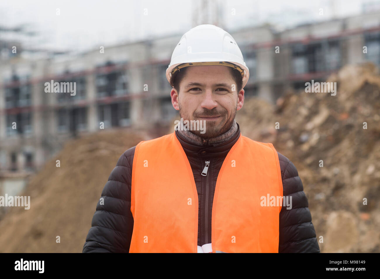 Ritratto di contenuto uomo che indossa giubbotto di sicurezza e casco al sito in costruzione Foto Stock