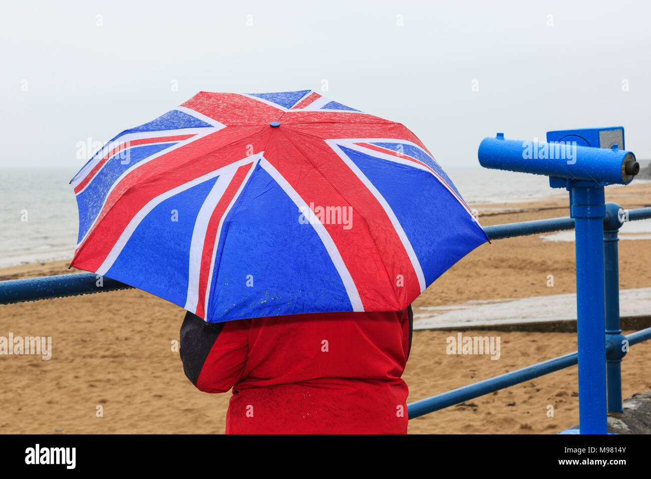 Una persona che si affaccia al mare sul lungomare di deserte località balneare con una Unione Jack ombrello durante molto bagnato estate britannica meteo. Anglesey Wales UK Foto Stock