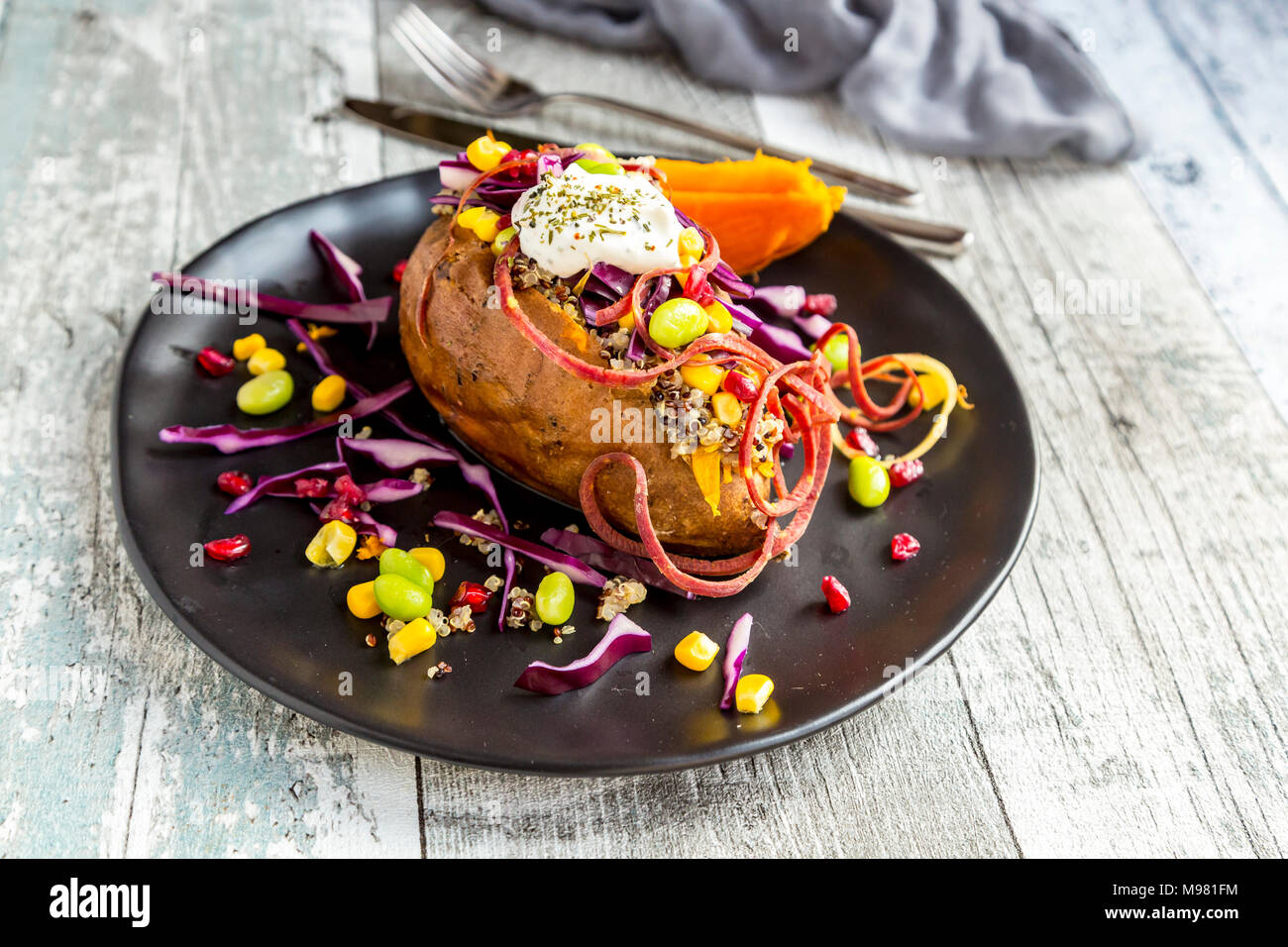 Kumpir, riempito sweet potatoe, cavolo rosso, mais, edamame, carote, quinoa, crème fraiche sulla piastra Foto Stock
