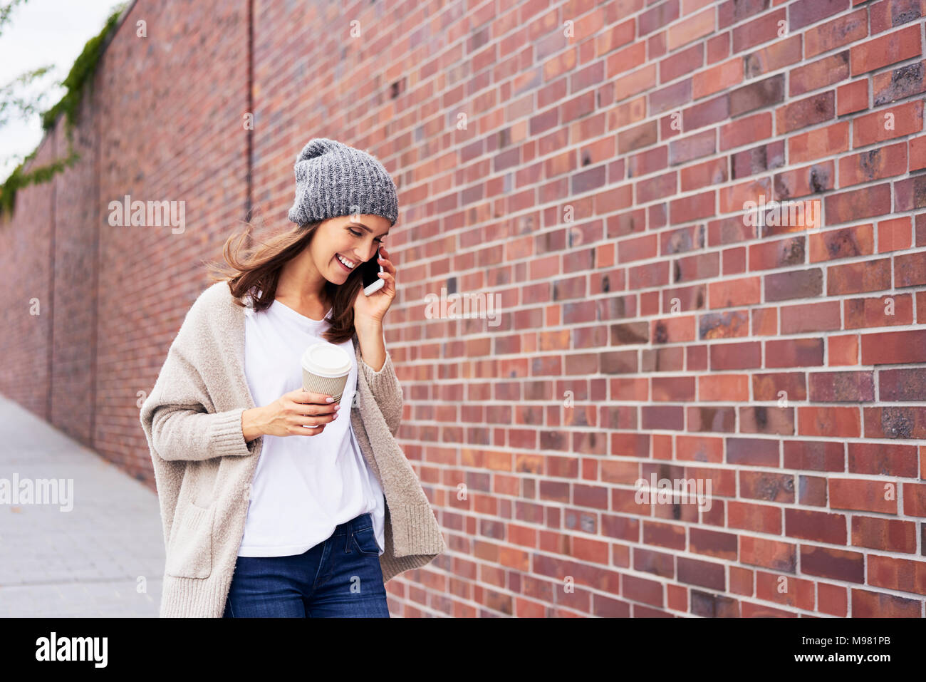 Donna felice con caffè per andare al telefono Foto Stock