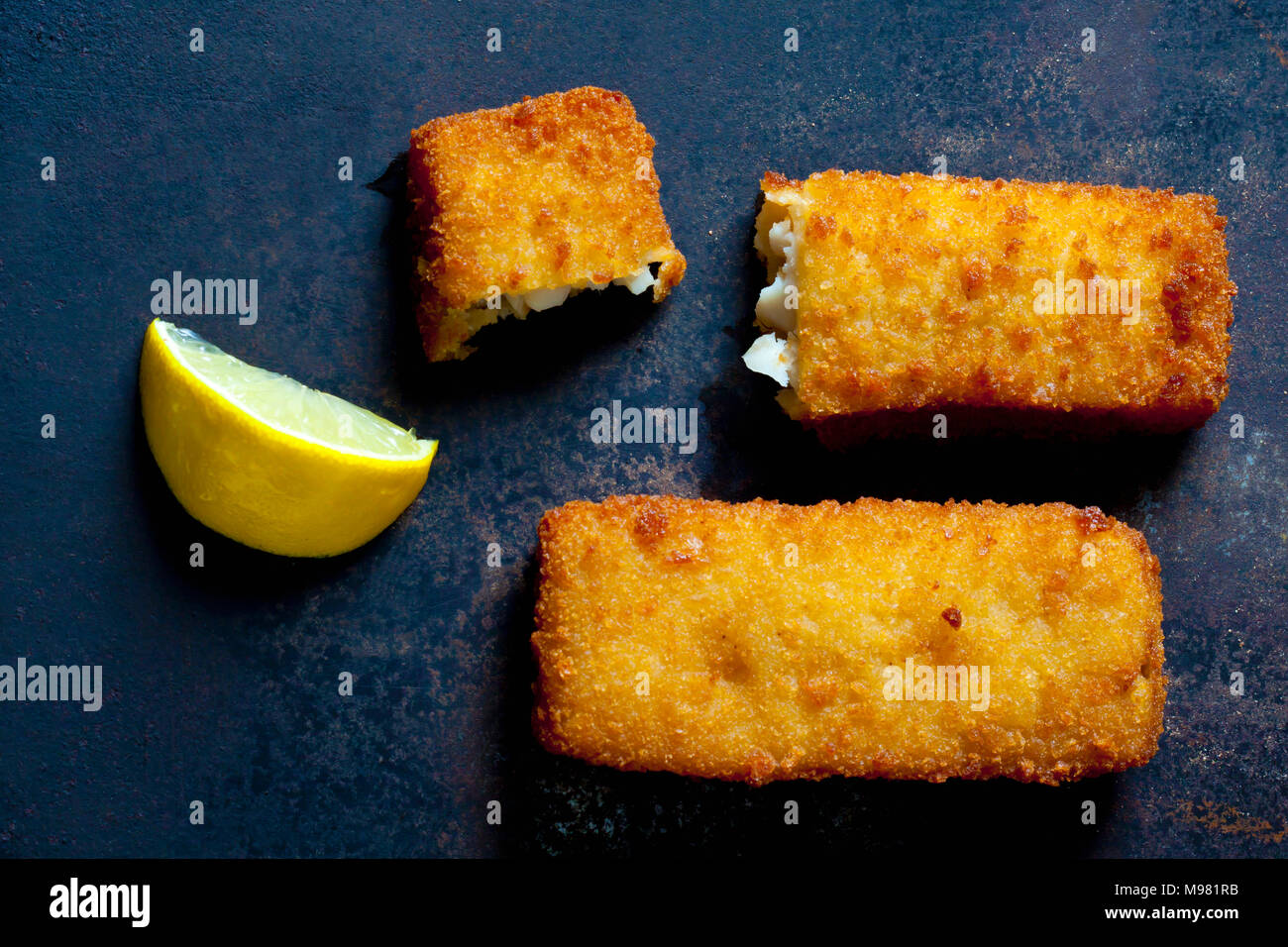 I bastoncini di pesce e la fetta di limone su metallo scuro Foto Stock