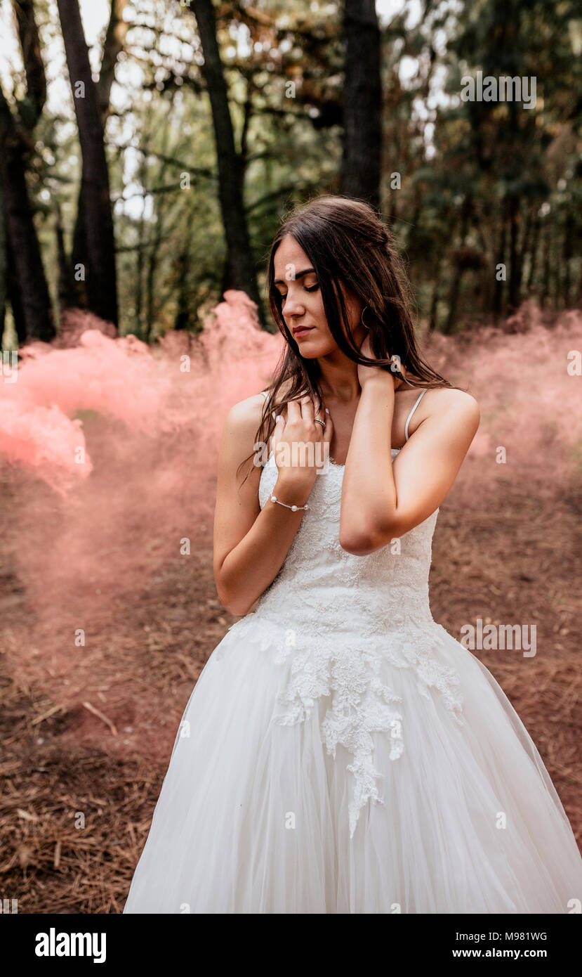Donna con gli occhi chiusi che indossa abiti da sposa nella foresta circondato da nuvole di fumo Foto Stock