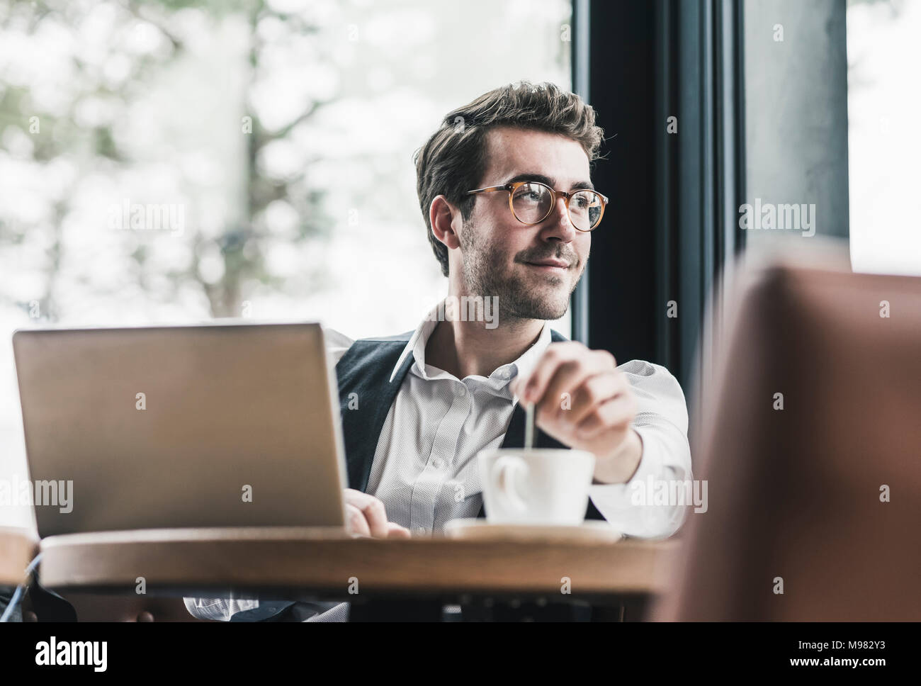 Sorridente giovane in un cafe con il computer portatile e la tazza di caffè Foto Stock