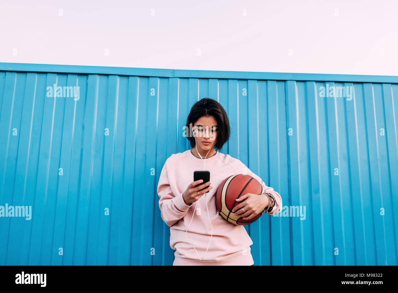 Giovane donna con basket, smartphone e gli auricolari in corrispondenza del recipiente Foto Stock