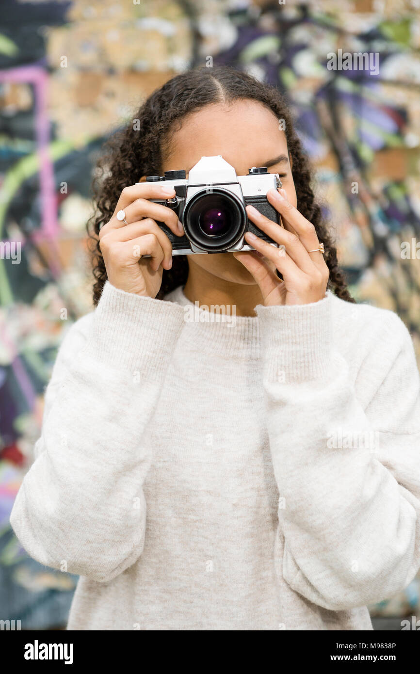 Germania, Berlino, giovane donna di scattare foto con una vecchia fotocamera nella parte anteriore del graffiti Foto Stock