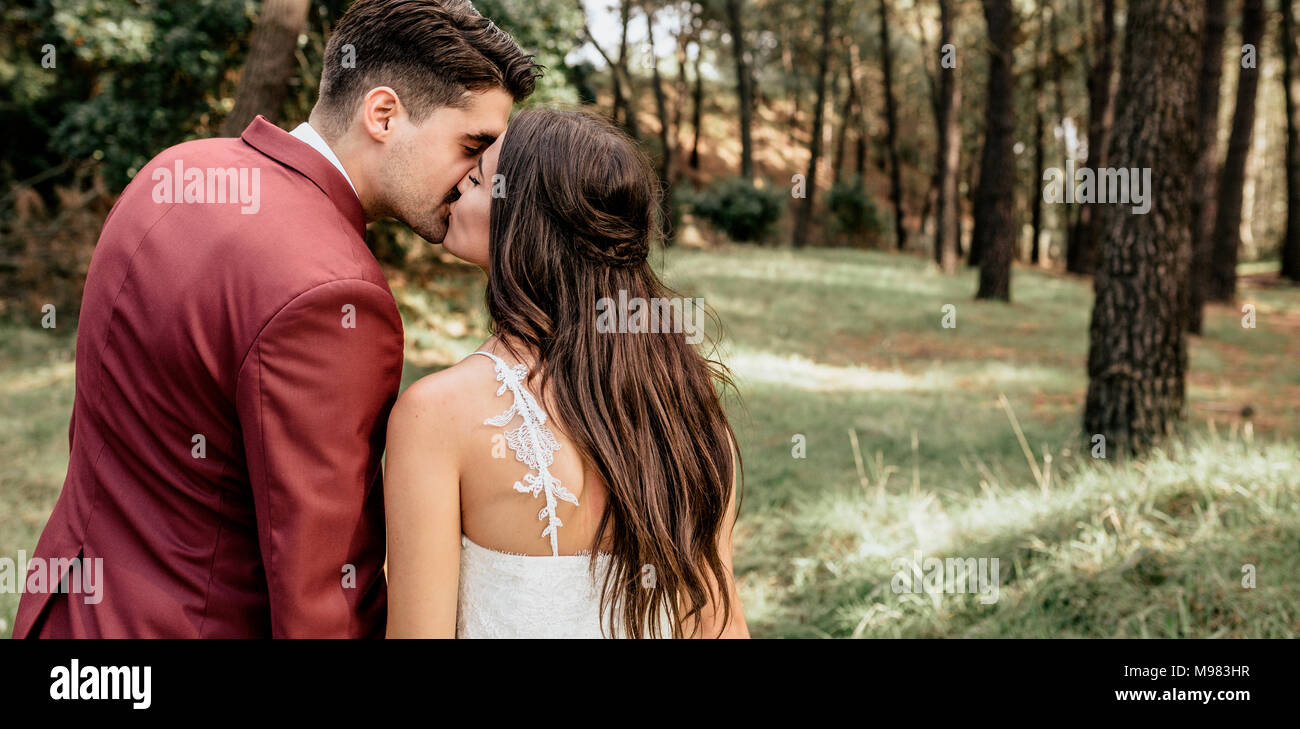 Vista posteriore della sposa e lo sposo baciare in foresta Foto Stock