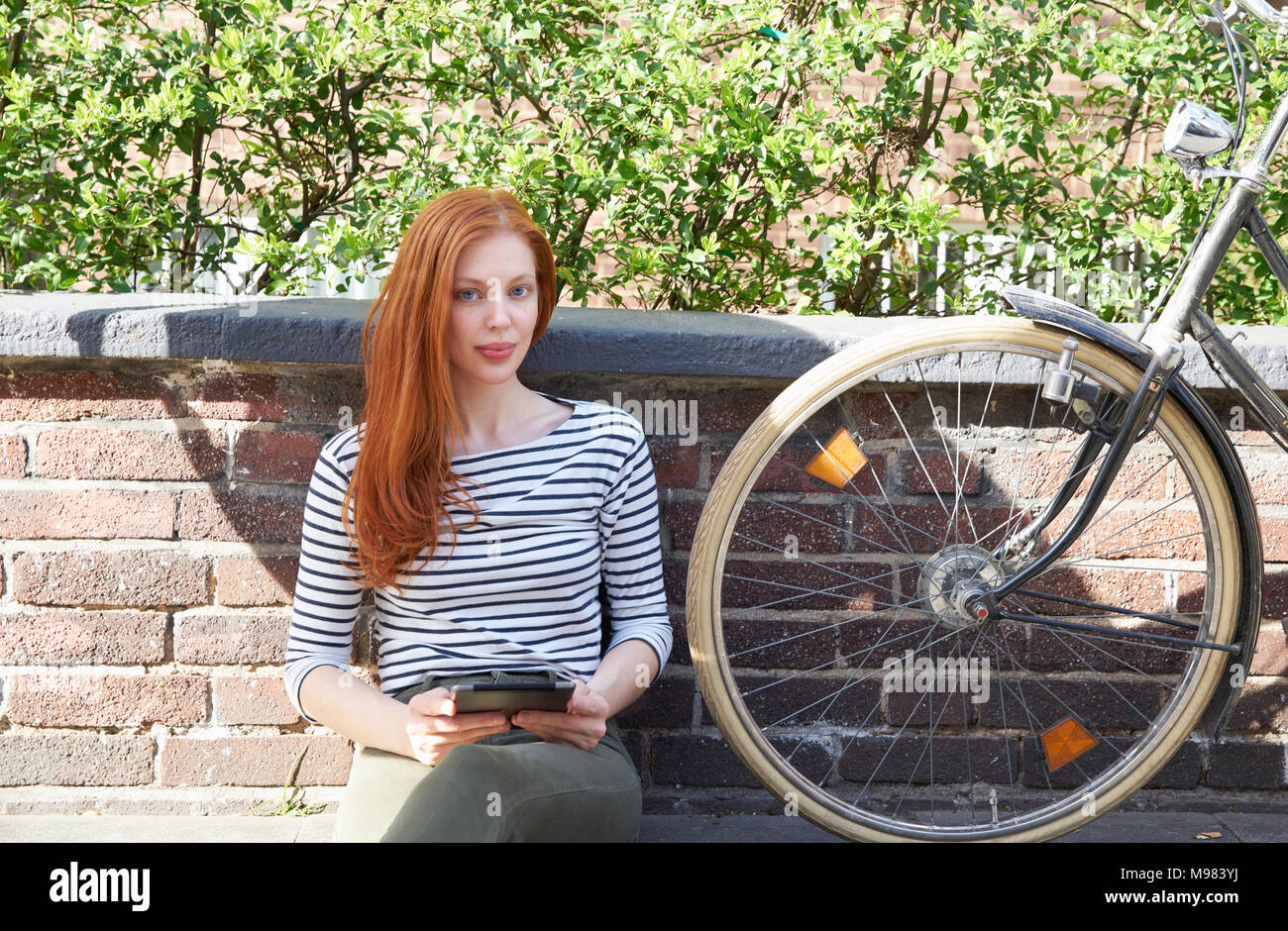 Ritratto di donna redheaded con tavoletta e di biciclette seduto su una parete Foto Stock