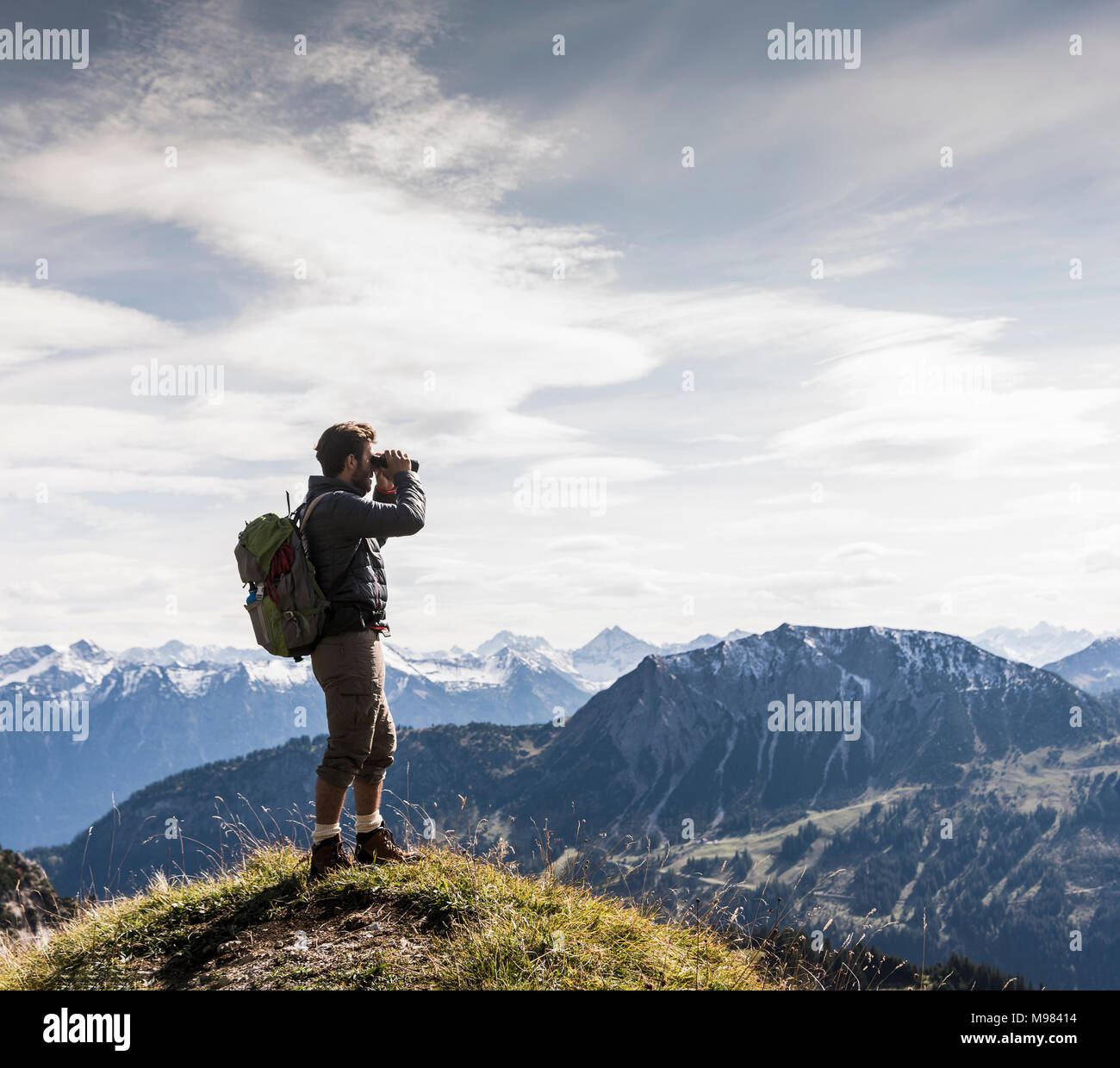 Austria, Tirolo, giovane uomo in piedi in mountainscape guardando a vista con il binocolo Foto Stock