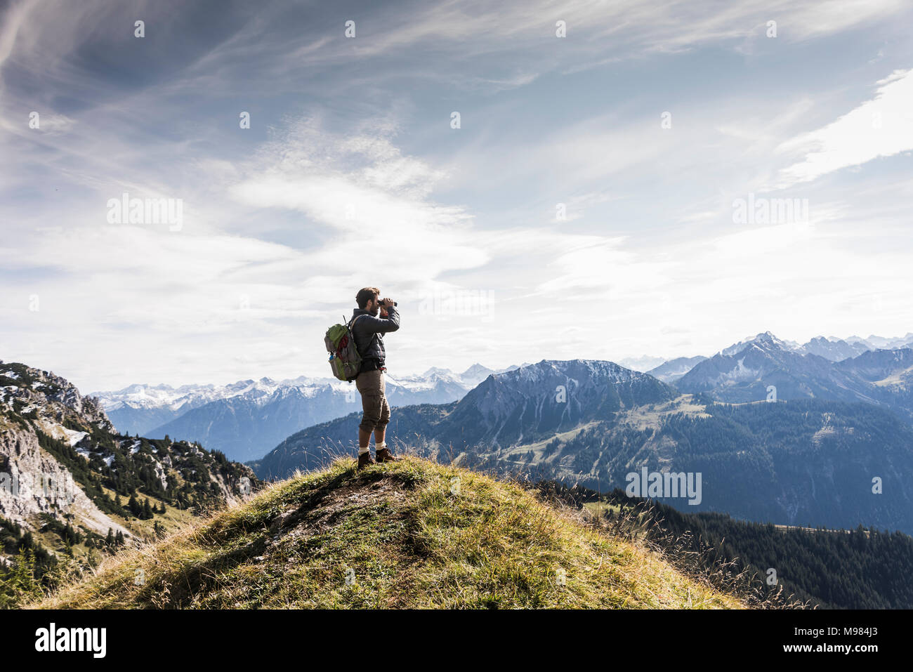 Austria, Tirolo, giovane uomo in piedi in mountainscape guardando a vista con il binocolo Foto Stock