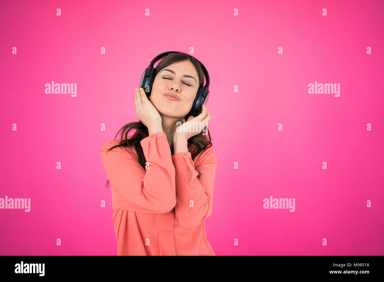 Donna di fronte a parete rosa ascoltando musica sulle cuffie Foto Stock