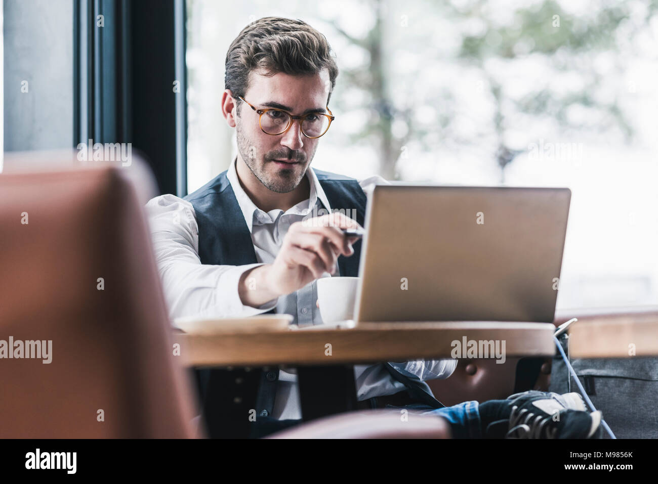 Giovane uomo che lavora in un cafe utilizzando laptop e prendere note Foto Stock