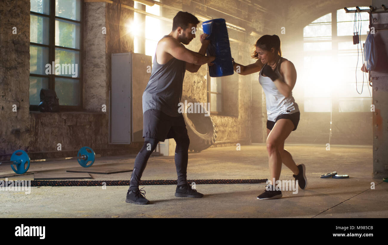 Athletic donna Hits sacco da boxe che il suo partner/ Trainer tiene. Lei è professionale e combattente è la formazione in una palestra. Foto Stock