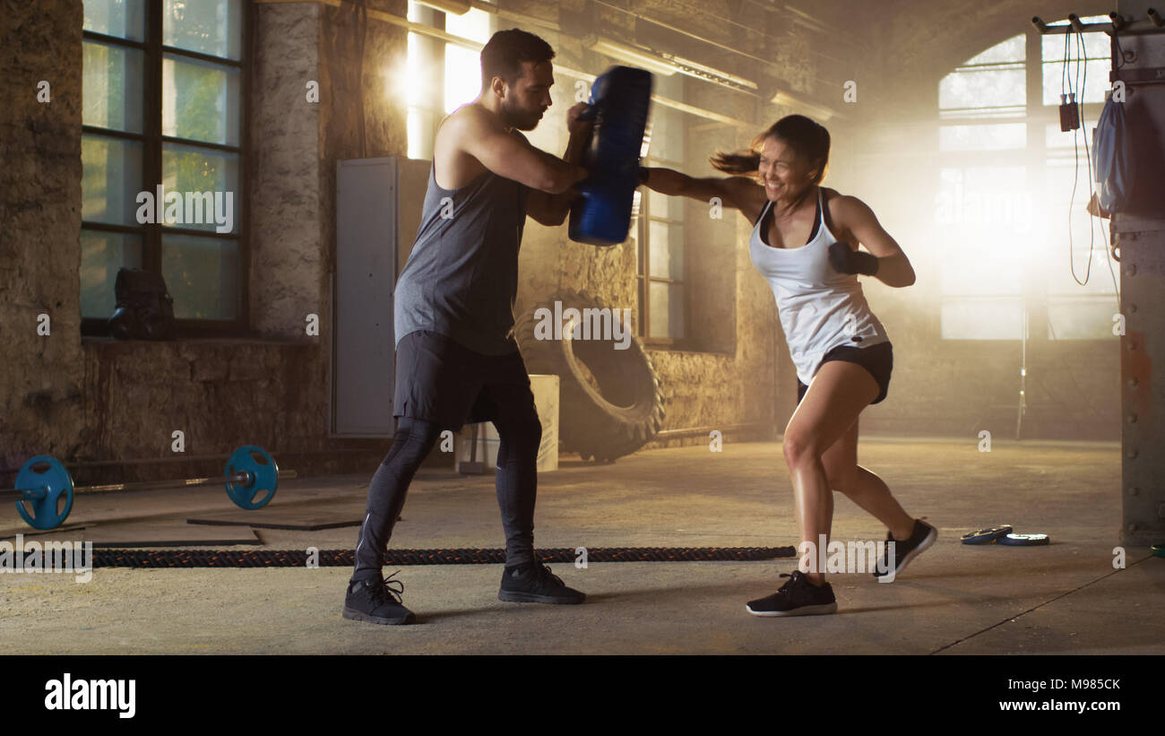 Athletic donna Hits sacco da boxe che il suo partner/ Trainer tiene. Lei è professionale e combattente è la formazione in una palestra. Foto Stock
