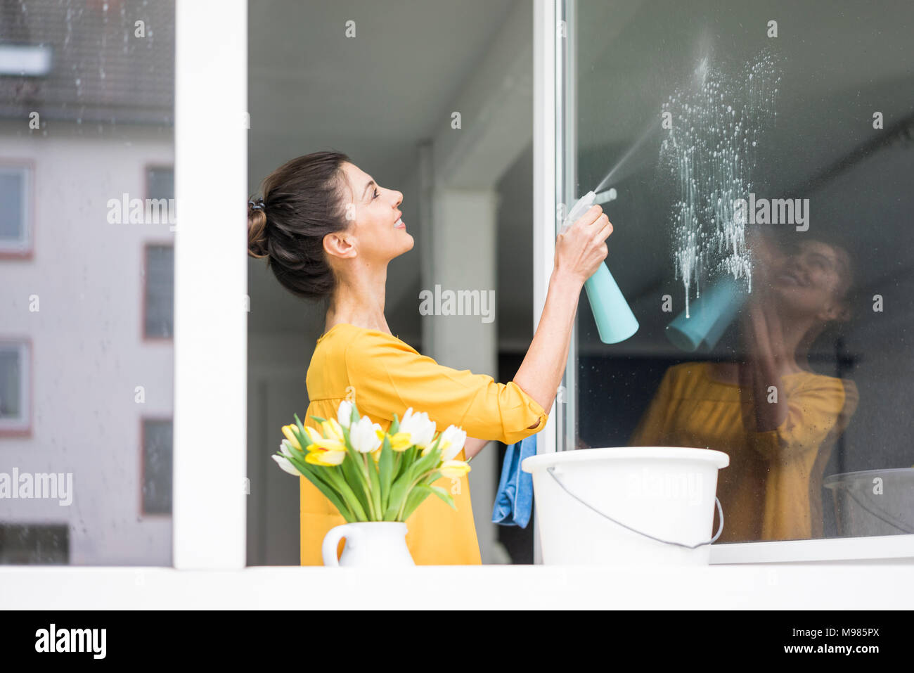 Donna sorridente a casa pulizia del vetro Foto Stock