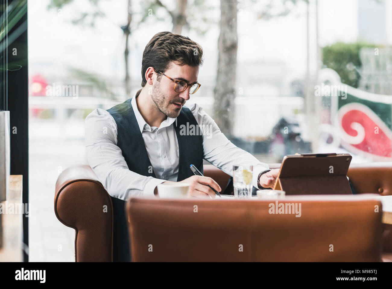 Giovane uomo che lavora in un bar con tablet e prendere note Foto Stock