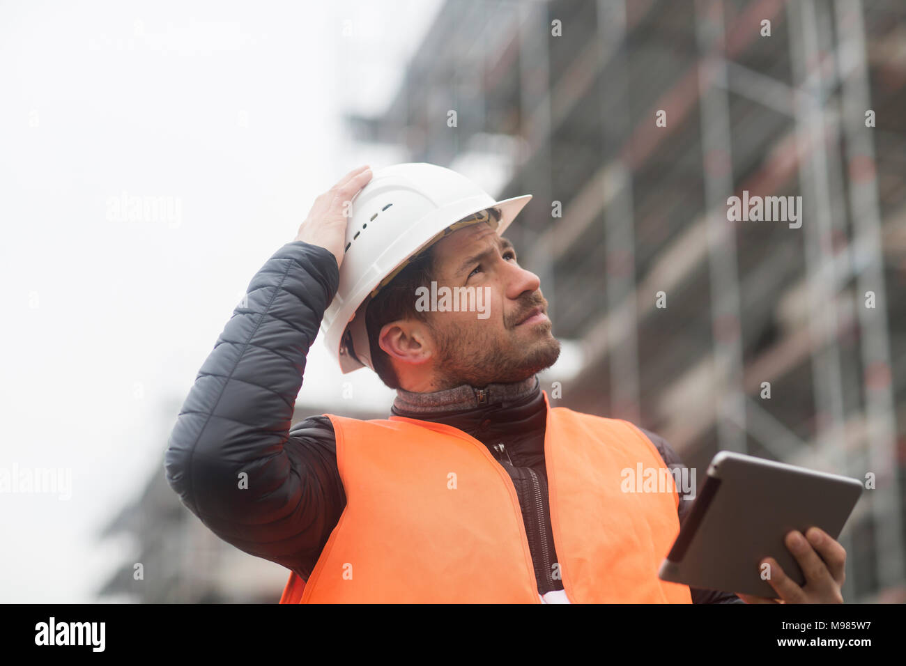 L'uomo con la compressa indossare giubbotto di sicurezza e di elmetto in sito in costruzione Foto Stock