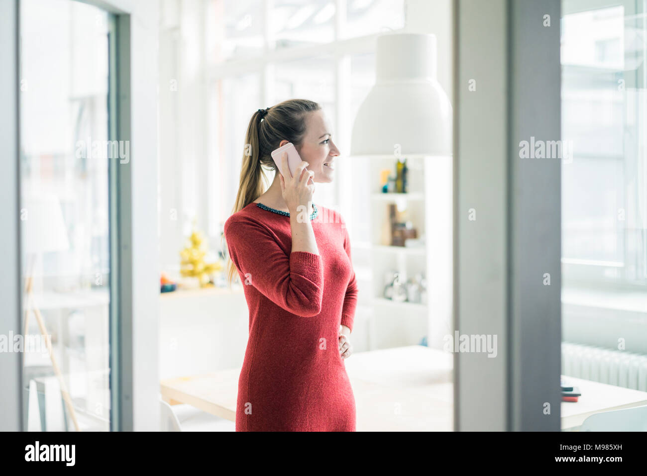 Donna sorridente al telefono guardando fuori della finestra Foto Stock
