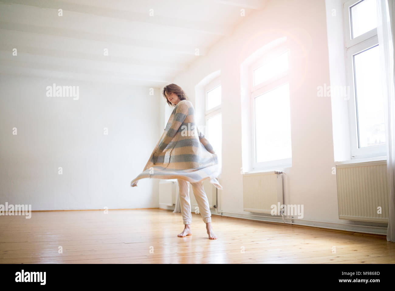 Felice donna matura in piedi nella stanza vuota nella luce solare Foto Stock