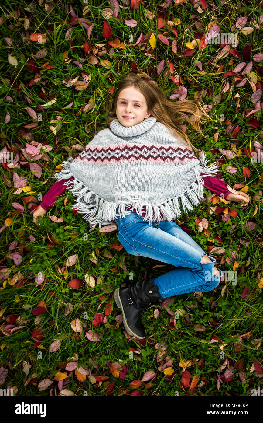 Ritratto di ragazza sorridente che indossa il poncho giacente sul prato autunnale Foto Stock
