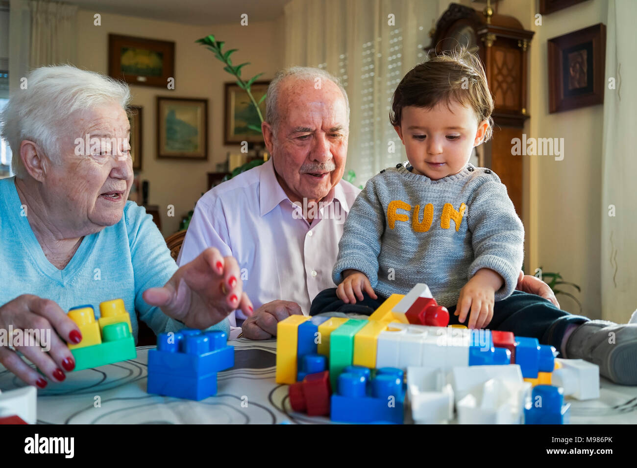 Grande-nonni e baby girl insieme giocando in plastica con mattoni di edificio a casa Foto Stock