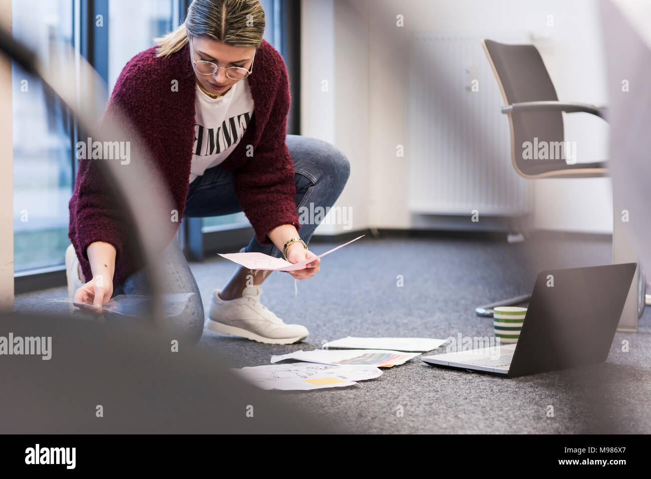 Giovane donna con il computer portatile e i documenti di lavoro sul pavimento in ufficio Foto Stock
