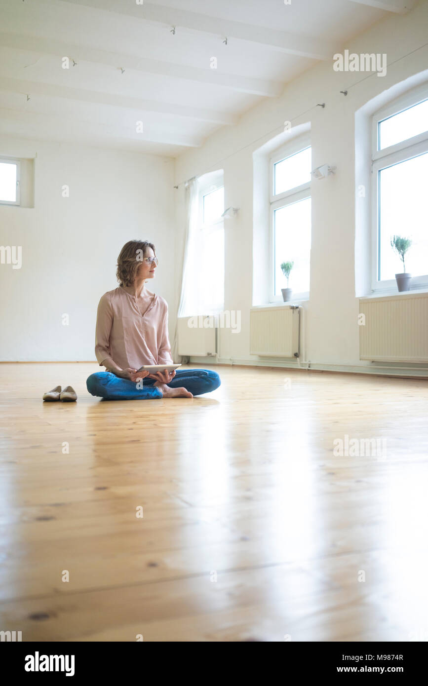 Donna matura seduti sul pavimento in camera a vuoto con la compressa Foto Stock