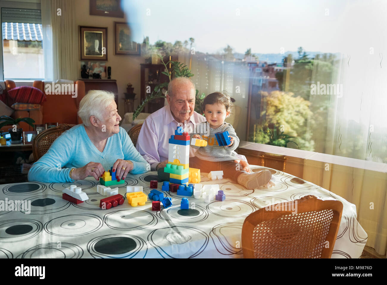 Grande-nonni e baby girl insieme giocando in plastica con mattoni di edificio a casa Foto Stock