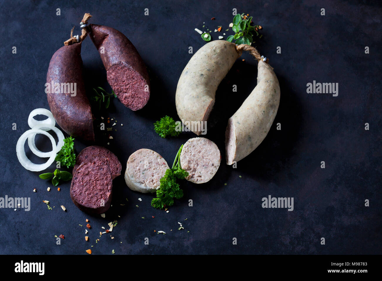 Fette di salsicce di fegato e salsicce di sangue, anelli di cipolla, prezzemolo e erbe sul terreno scuro Foto Stock