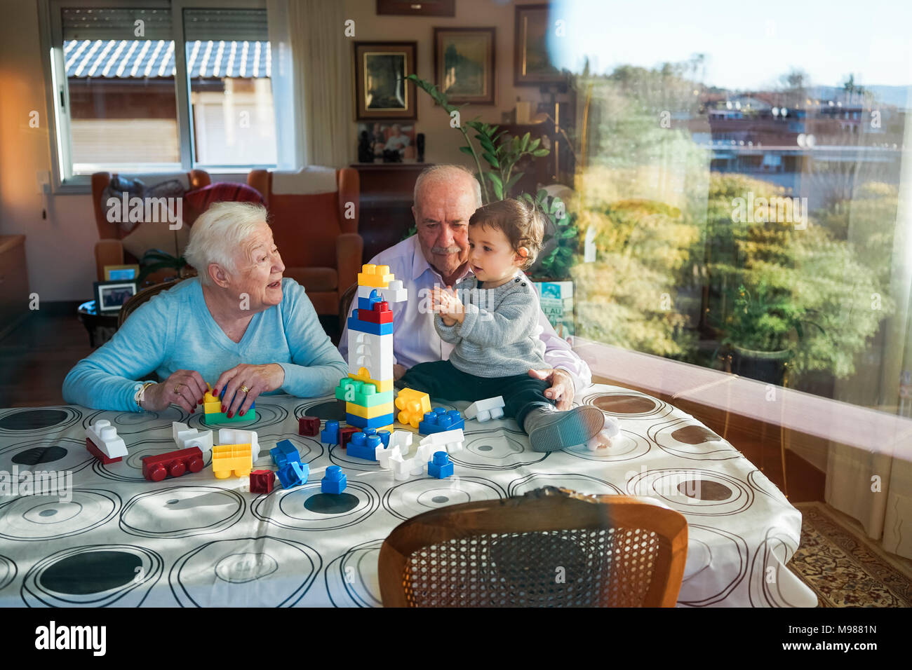 Grande-nonni e baby girl insieme giocando in plastica con mattoni di edificio a casa Foto Stock