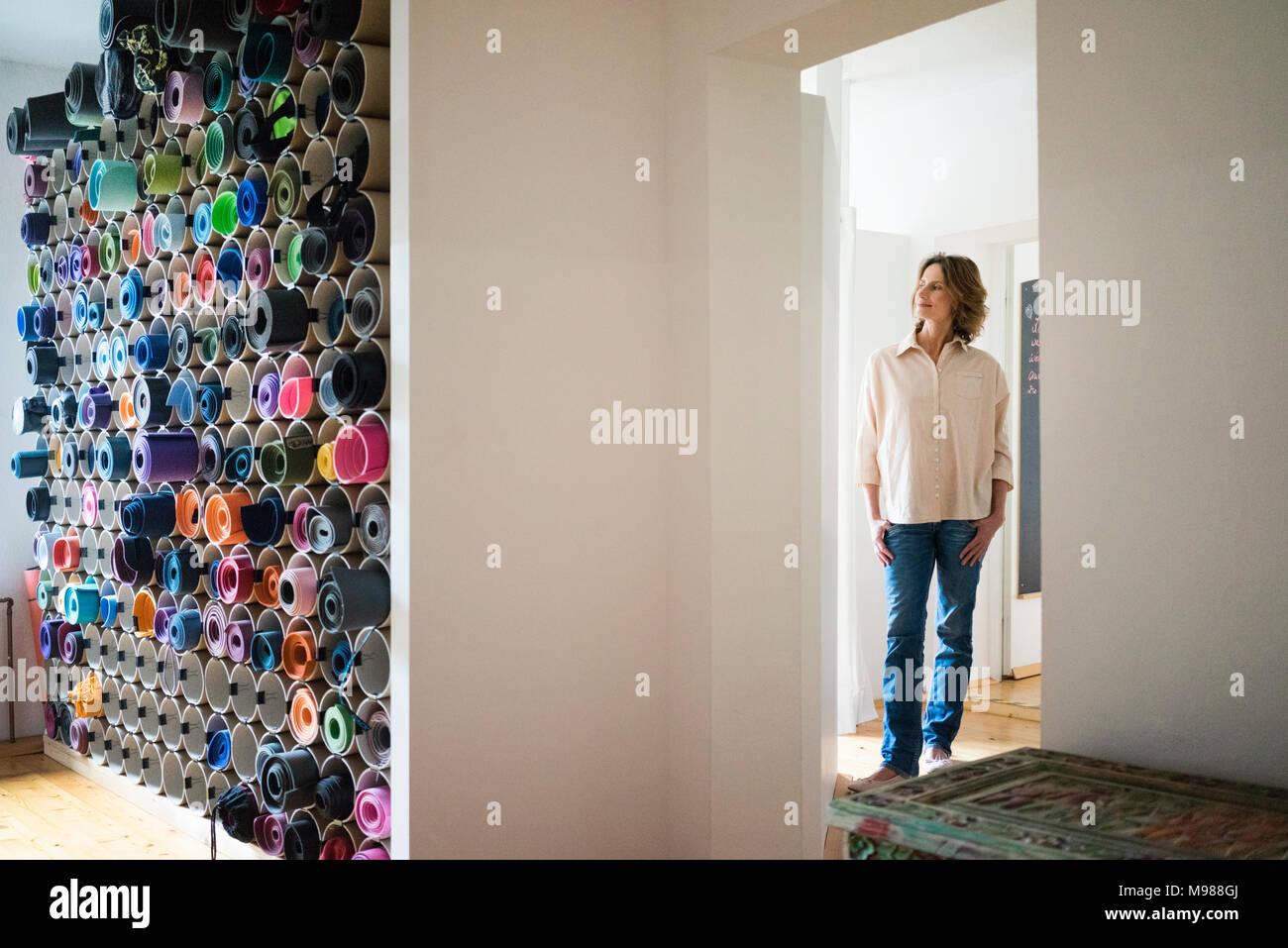 Donna matura in una stanza con un vasto assortimento di tappeti di yoga Foto Stock