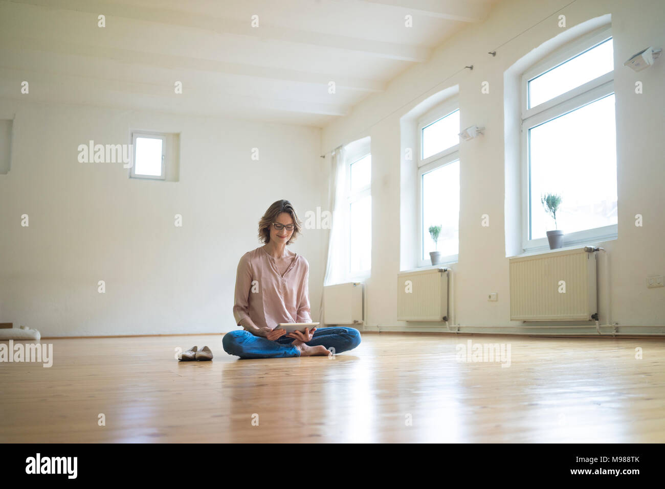 Donna matura seduta sul pavimento nella stanza vuota utilizzando tablet Foto Stock