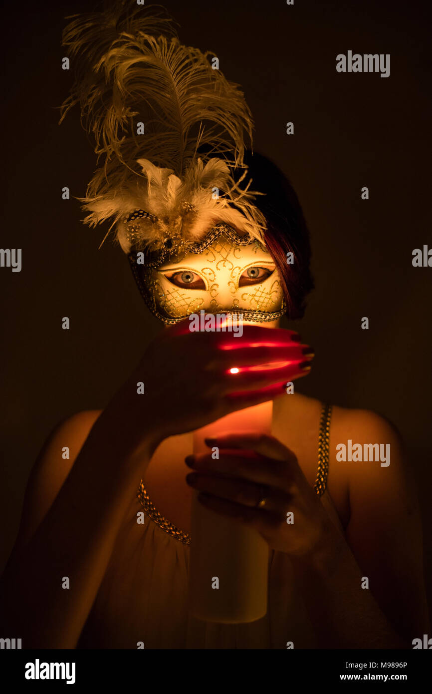 Mantenendo segreti: una ragazza donna che indossa un elaborato ballo maschera per nascondere la sua identità, la coppettazione la sua mano attorno alla fiamma di una candela Foto Stock