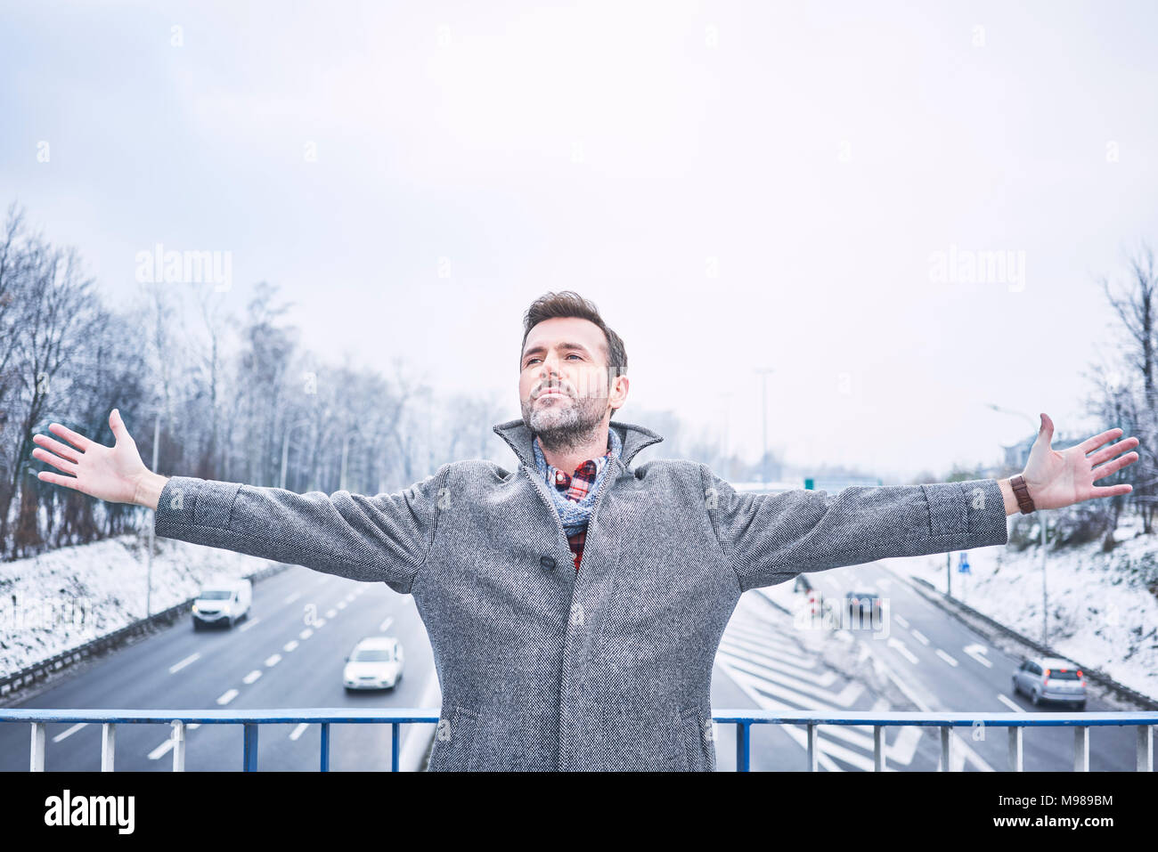 Ritratto di uomo con le braccia aperte in piedi sul ponte sopra l'autostrada Foto Stock